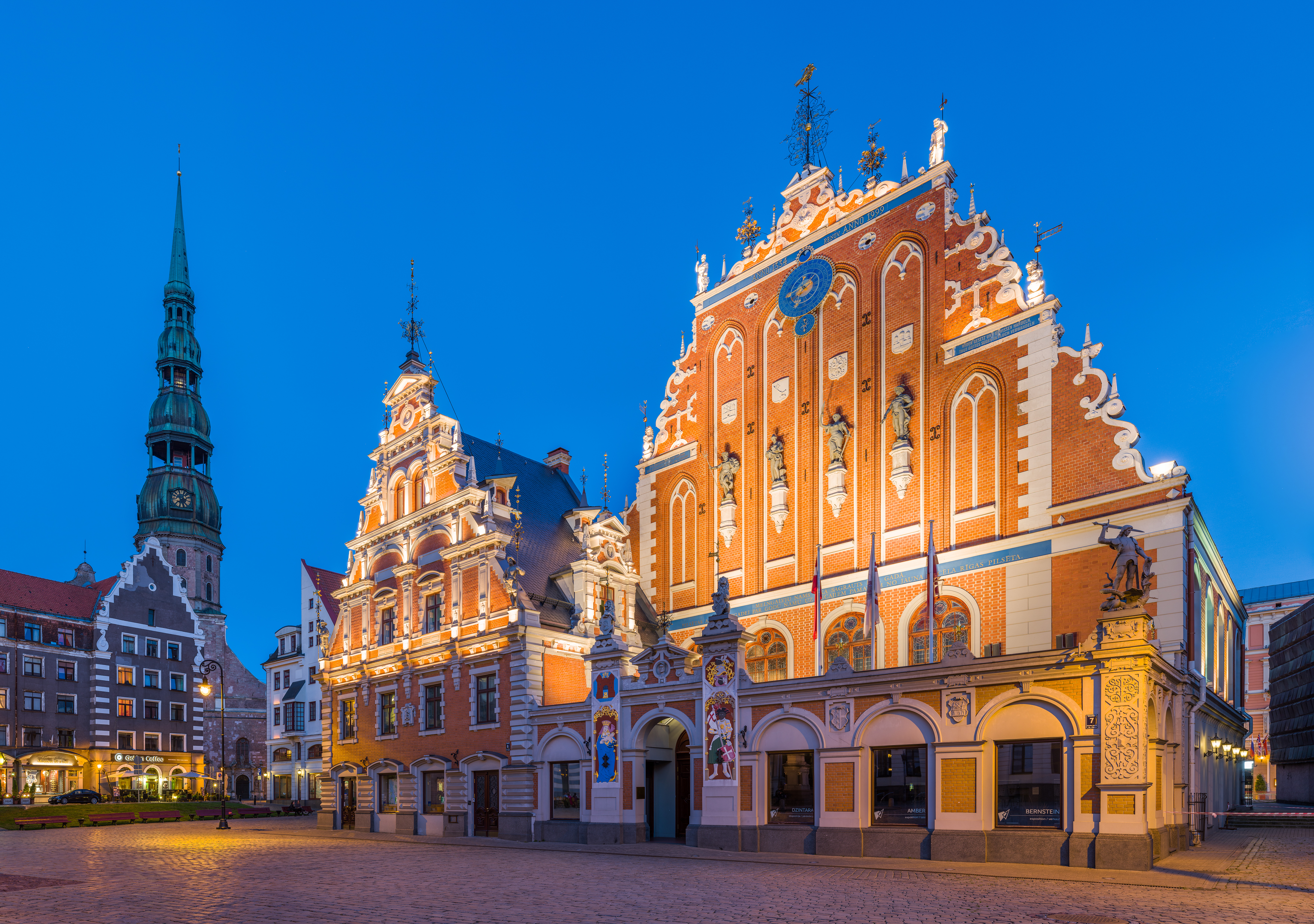 The House of the Blackheads in Riga at blue hour, its red-brick stepped gable floodlit and covered in statues, clocks and coats of arms, with the green spire of St Peter's church behind it