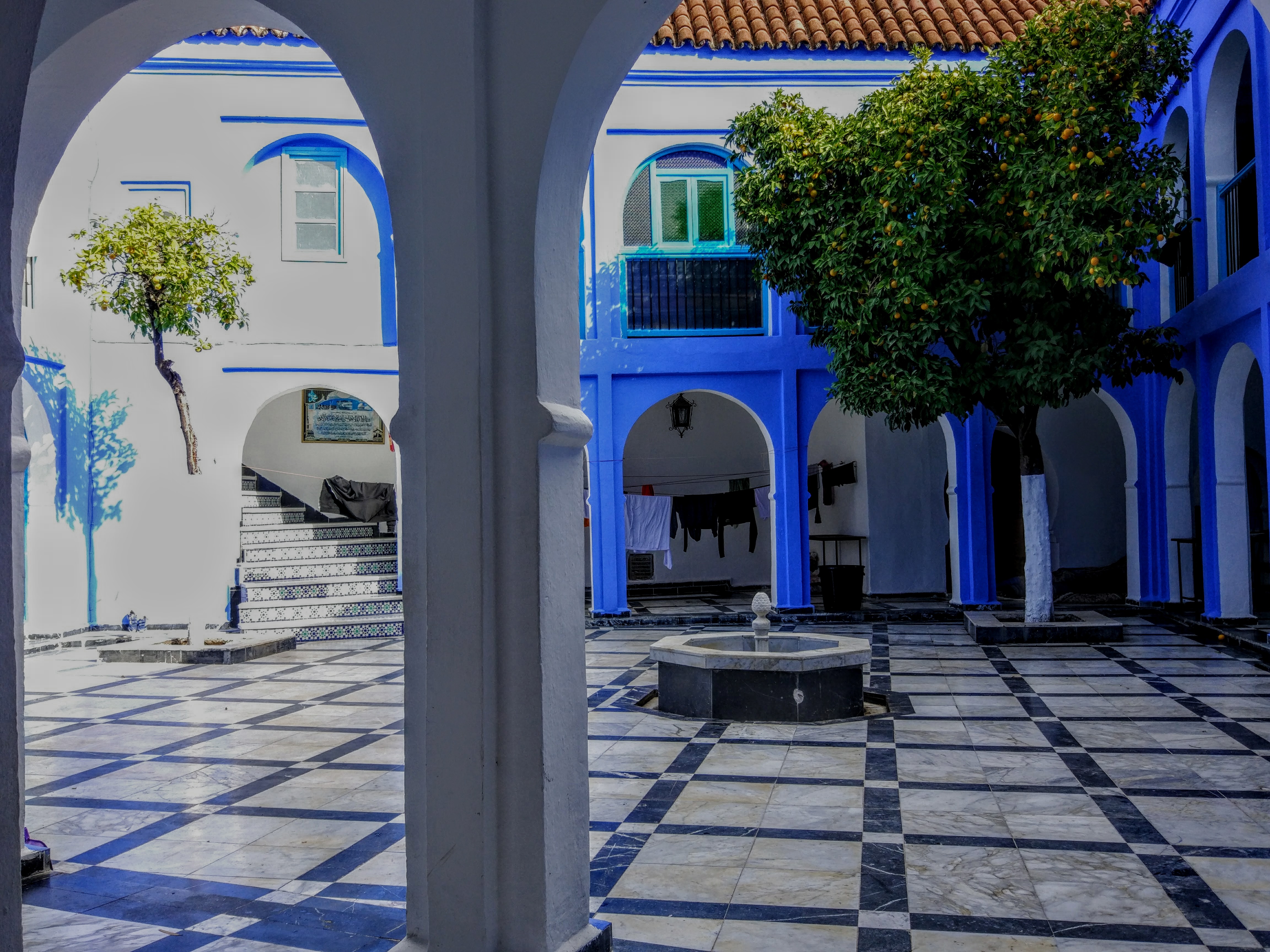 A blue-and-white courtyard in Chefchaouen with checkered marble floor, orange tree, and fountain